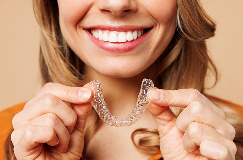 Nose-to-shoulder view of woman smiling holding Invisalign
