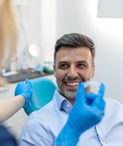 Man in dental chair smiling at dentist holding Invisalign in her gloved hand