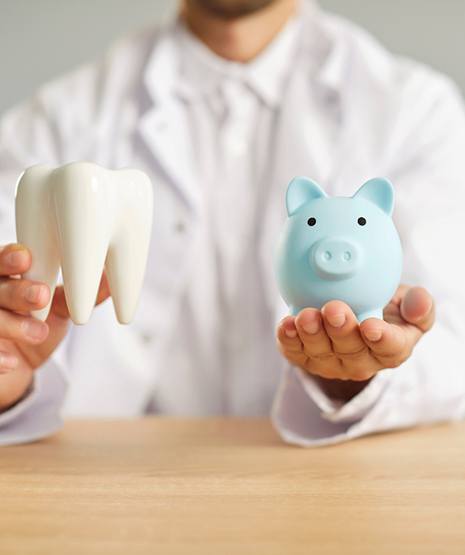 Dentist holding model tooth and blue piggy bank