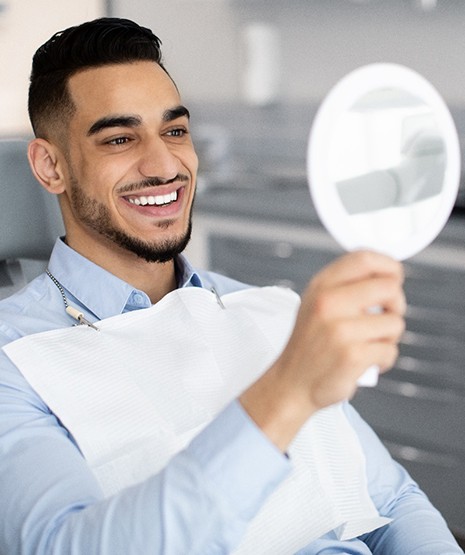 Young man in dental chair smiling at reflection in mirror
